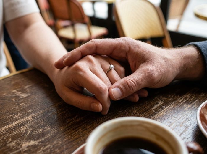 Gros plan de deux mains enlacées avec une bague de fiançailles solitaire diamant sur une table en bois