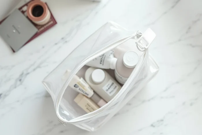 Vue aérienne d'un sac plastique transparent réglementaire avec dentifrice et cosmétiques en format voyage pour le bagage cabine